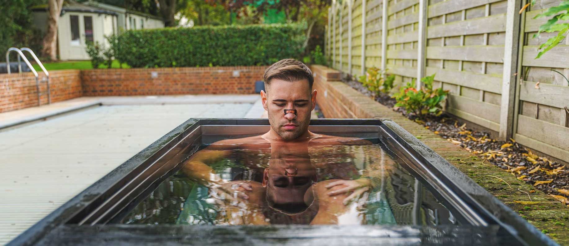 A young man sitting in chill tubs ice bath in a UK garden