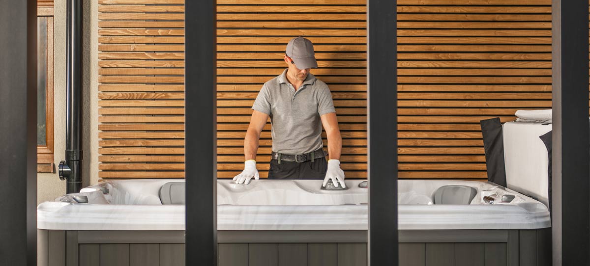 A workman in a grey cap and grey polo shirt, wearing white gloes, performing maintenance on a hot tub