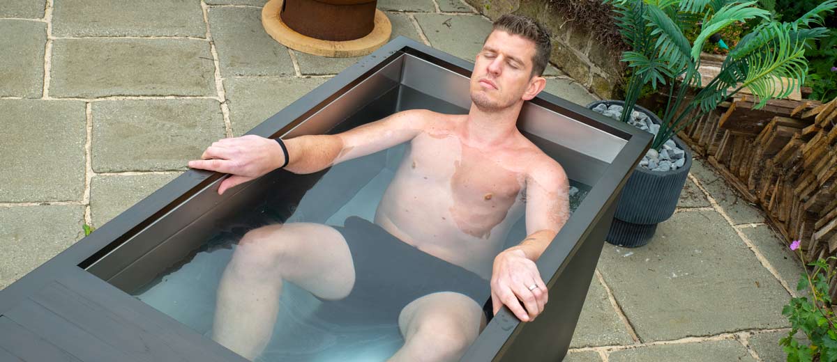 An atheletic looking man laying in a premium Chill Tubs ice bath in a garden setting