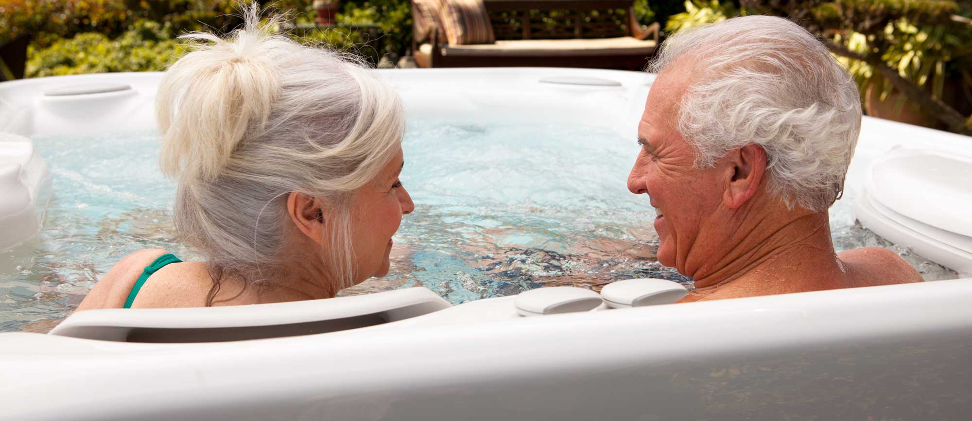 An older couple in a hot tub, seen from behind, looking at each other affectionately