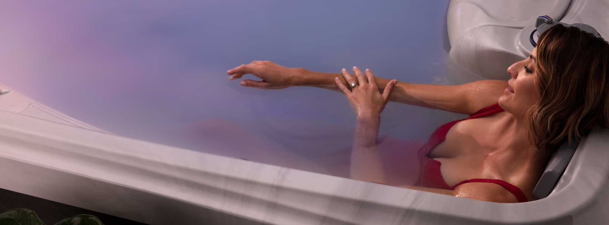 A woman in a red bathing suit relaxing in a the milky-white water of a MicroSilk-enabled hot tub