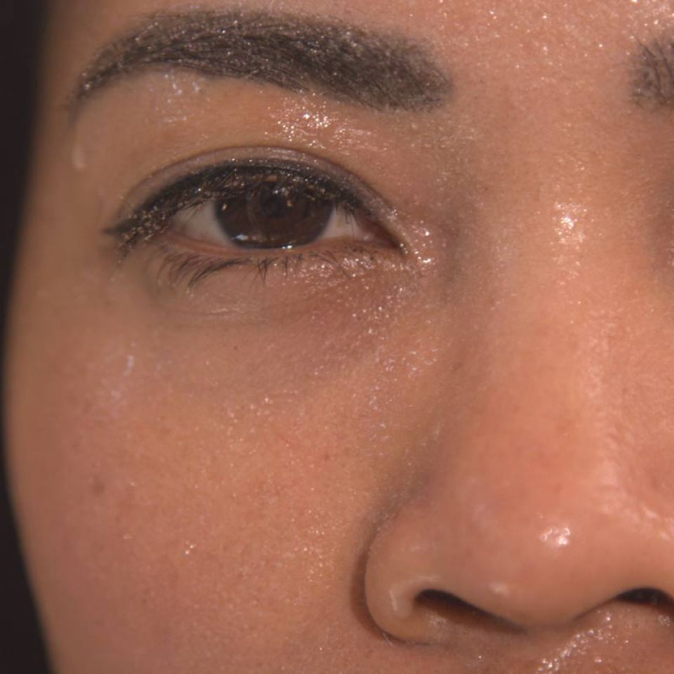 Close up of a woman's face covered in sweat, showing one eye, cheek and nose