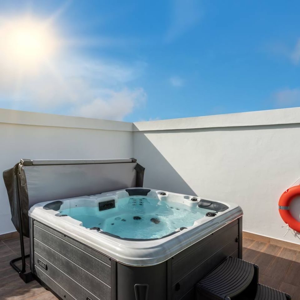 A hot tub in a minimalist garden surrounded by two adjacent white walls, upon one if which is a life ring