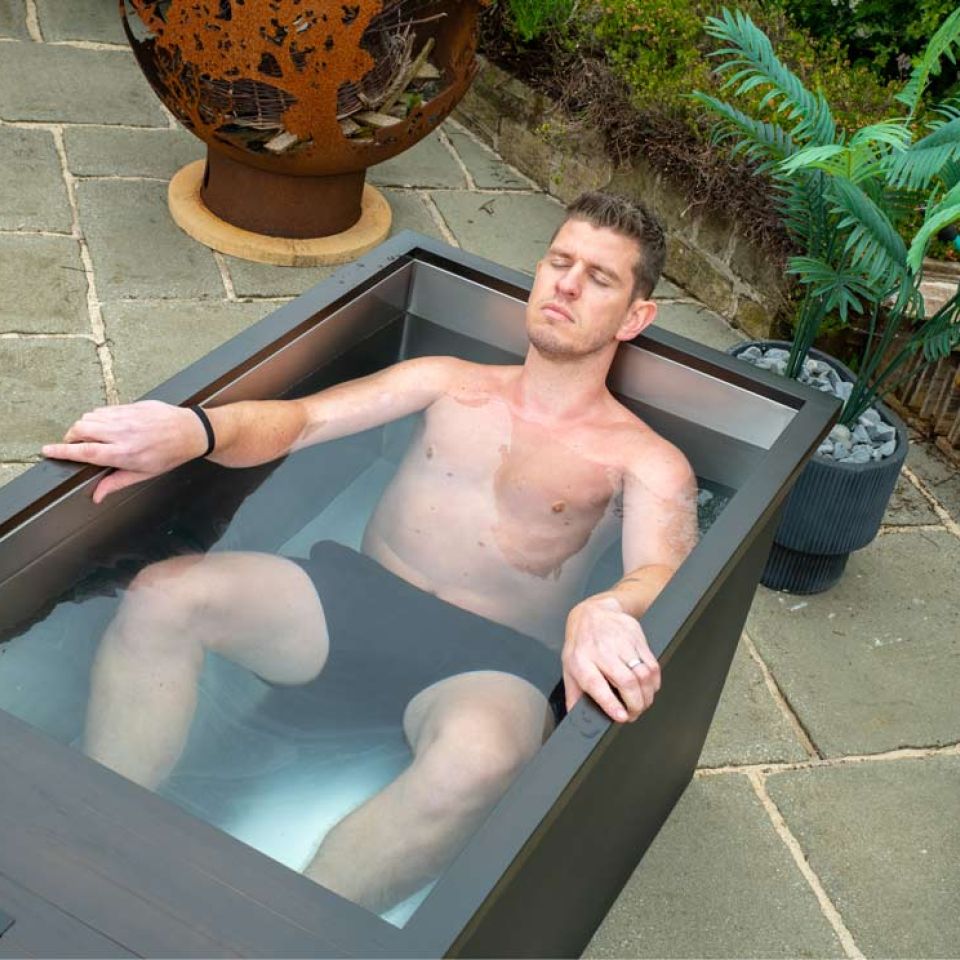 An atheletic looking man laying in a premium Chill Tubs ice bath in a garden setting