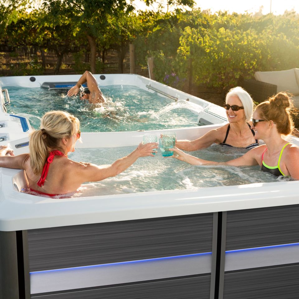 Women toasting in swim spa while man swims