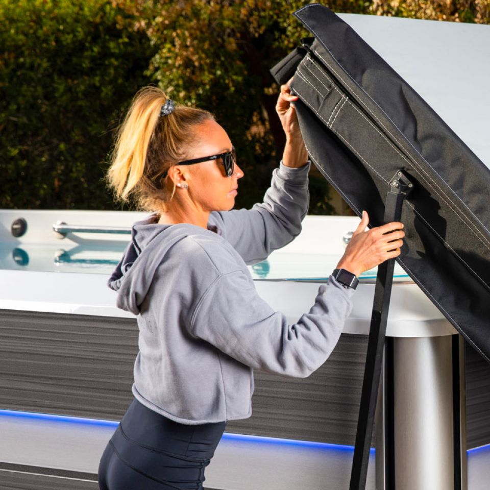 A young woman in fitness clothes opening the cover on an endless pool swim spa