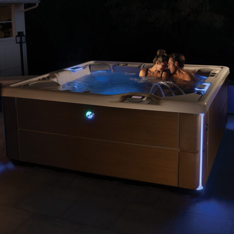 A couple enjoying the Highlife Vanguard together on a patio in the night. The tub is illuminated by led lighting and the effect is quite romantic